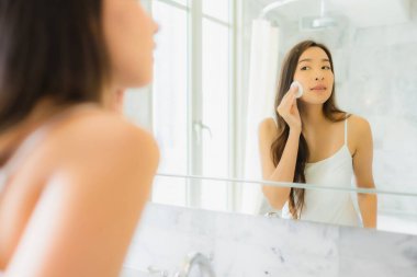 Güzel bir Asyalı kadın portresi. Banyo içerisindeki aynada yüzünü kontrol et ve makyaj yap.