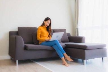Genç Asyalı bir kadının oturma odasında çalışmak için dizüstü bilgisayar defteri kullanmasının portresi.