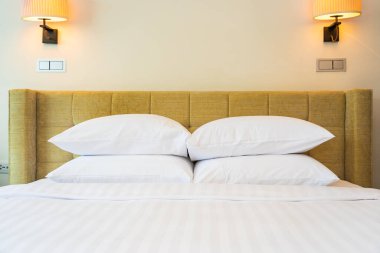 Yatak odasının içinde lamba süslemesi olan beyaz yastık ve battaniye.