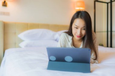 Güzel bir Asyalı kadının portresi yatak odasının içinde kredi kartıyla tablet kullanıyor.