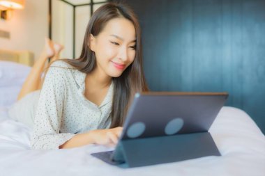 Güzel bir Asyalı kadının portresi yatak odasının içinde kredi kartıyla tablet kullanıyor.