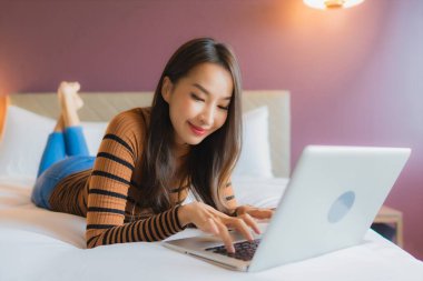 Asyalı güzel bir kadının portresi yatak odasının iç kısmında kredi kartıyla birlikte dizüstü bilgisayar kullanıyor.