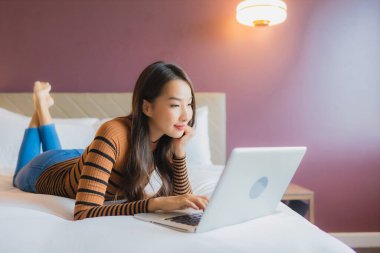 Asyalı güzel bir kadının portresi yatak odasının iç kısmında kredi kartıyla birlikte dizüstü bilgisayar kullanıyor.