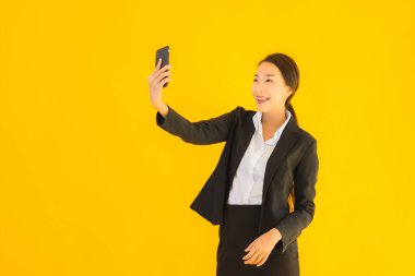 Portre güzel genç Asyalı kadın akıllı cep telefonu ve kahve fincanı ile izole edilmiş sarı arka planda