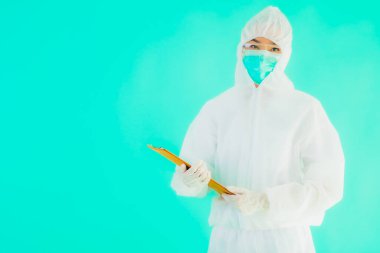Güzel, genç Asyalı doktor kadın koronavirüsten korunmak için ppe ya da kişisel koruyucu ekipman takıyor ya da mavi izole arka planda beyaz kartı olan 19. bölgede yaşıyor.