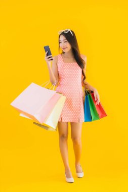 Renkli alışveriş çantalı güzel Asyalı kadın akıllı cep telefonu ve sarı izole edilmiş arka planda kredi kartı.