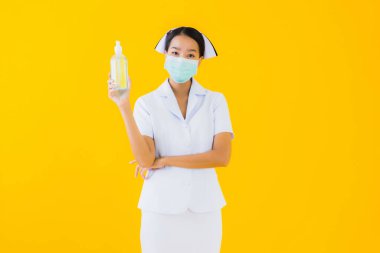 Asyalı güzel bir kadının portresi. Taylandlı hemşire, kovid19 ya da koronavirüsü korumak için maske takıyor ve sarı arka planda alkol jeli gösteriyor.