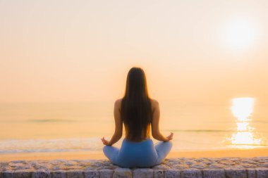 Genç Asyalı kadının portresi sağlık için gün doğumunda deniz kıyısı okyanusunda meditasyon yapıyor.