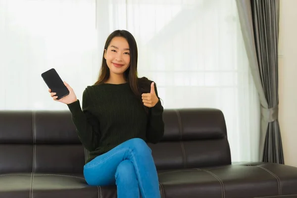 Portrait beautiful young asian woman use smart mobile phone or cellphone on sofa in living room interior