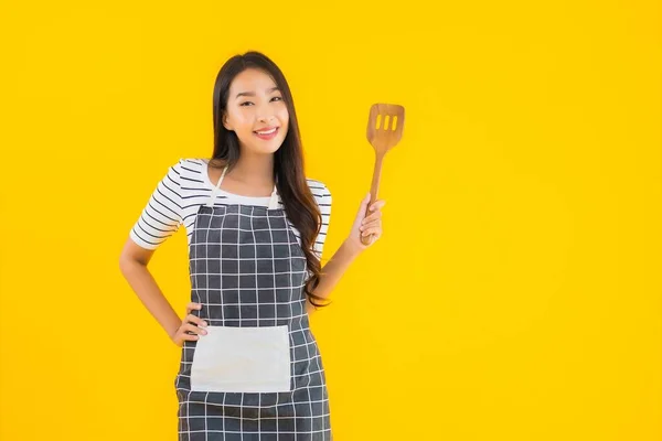 肖像画美しい若いアジアの女性は 黄色の隔離された背景に黒パンとSpatulaとエプロンを着用 — ストック写真