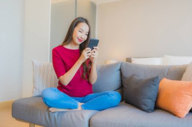 Güzel bir Asyalı kadın portresi. Yatak odasının iç tarafındaki oturma odasındaki koltukta akıllı cep telefonu kullanıyor.