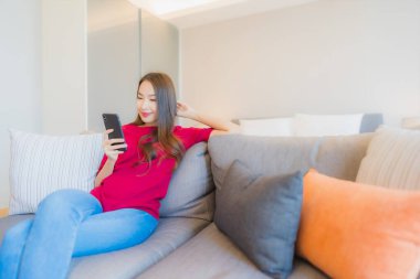 Güzel bir Asyalı kadın portresi. Yatak odasının iç tarafındaki oturma odasındaki koltukta akıllı cep telefonu kullanıyor.
