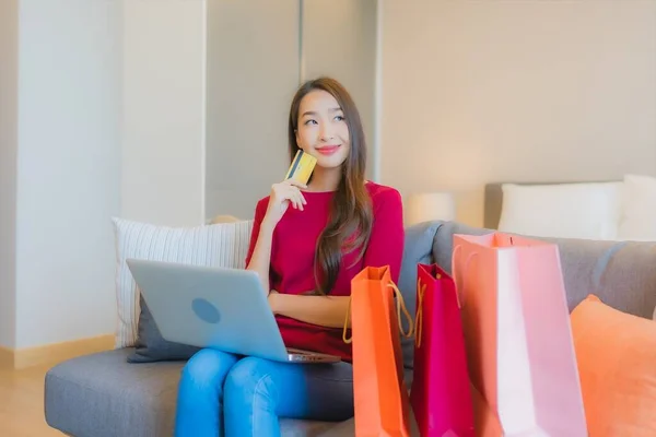 아시아 여성이 소파에 가방이 온라인 쇼핑용 카드가 노트북 컴퓨터를 사용하는 — 스톡 사진