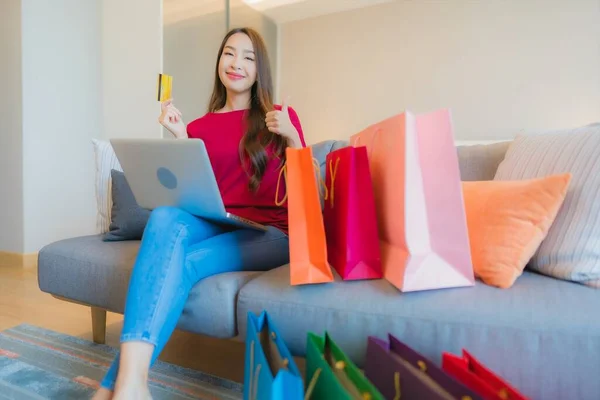 아시아 여성이 소파에 가방이 온라인 쇼핑용 카드가 노트북 컴퓨터를 사용하는 — 스톡 사진