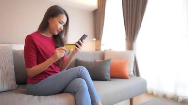 Güzel Asyalı bir kadının akıllı telefon ve kredi kartıyla e-alışveriş yaptığını gösteren görüntüler.