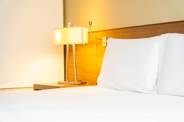 Yatak odasının içinde lamba süslemesi olan beyaz rahat yastık ve battaniye.