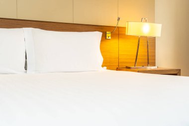 Yatak odasının içinde lamba süslemesi olan beyaz rahat yastık ve battaniye.