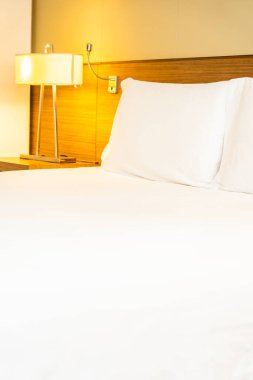 Yatak odasının içinde lamba süslemesi olan beyaz rahat yastık ve battaniye.