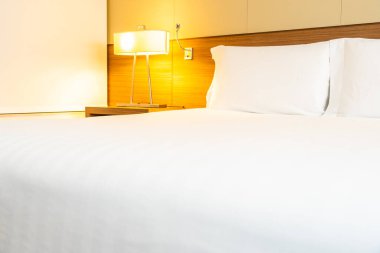 Yatak odasının içinde lamba süslemesi olan beyaz rahat yastık ve battaniye.