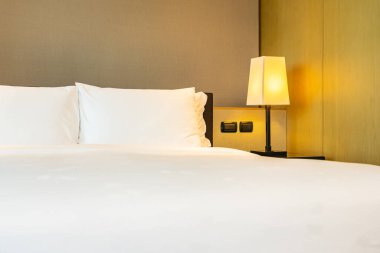 Yatak odasının içinde lamba süslemesi olan beyaz rahat yastık ve battaniye.