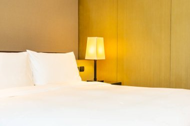 Yatak odasının içinde lamba süslemesi olan beyaz rahat yastık ve battaniye.