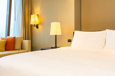 Yatak odasının içinde lamba süslemesi olan beyaz rahat yastık ve battaniye.