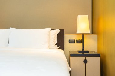 Yatak odasının içinde lamba süslemesi olan beyaz rahat yastık ve battaniye.