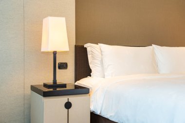 Yatak odasının içinde lamba süslemesi olan beyaz rahat yastık ve battaniye.