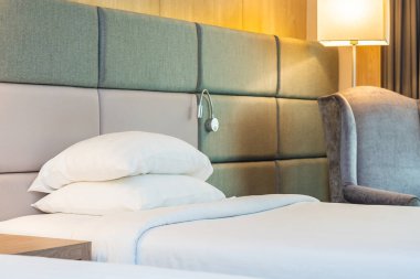 Yatak odasının içinde lamba süslemesi olan beyaz rahat yastık ve battaniye.