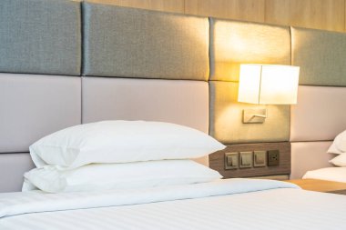 Yatak odasının içinde lamba süslemesi olan beyaz rahat yastık ve battaniye.