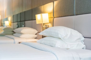 Yatak odasının içinde lamba süslemesi olan beyaz rahat yastık ve battaniye.