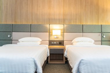 Yatak odasının içinde lamba süslemesi olan beyaz rahat yastık ve battaniye.