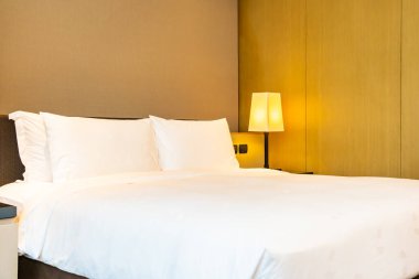 Yatak odasının içinde lamba süslemesi olan beyaz rahat yastık ve battaniye.