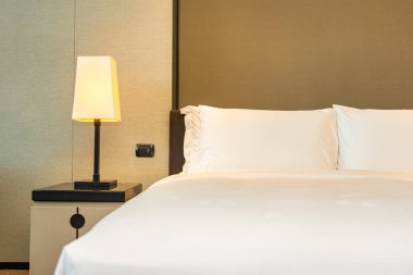 Yatak odasının içinde lamba süslemesi olan beyaz rahat yastık ve battaniye.