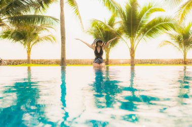 Güzel bir Asyalı kadın portresi, gün batımında palmiye ağacıyla birlikte havuz kenarında dinleniyor ya da tatil için gün doğumunda dinleniyor.