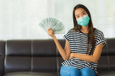 Maskeli güzel Asyalı kadının portresi evde para ya da para gösteriyor.