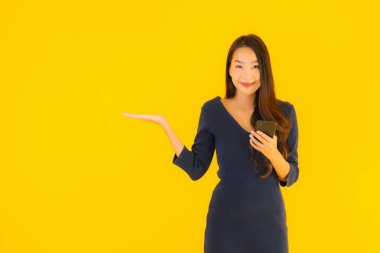 Akıllı cep telefonlu güzel Asyalı kadın portresi ya da sarı izole edilmiş arka planda cep telefonu.