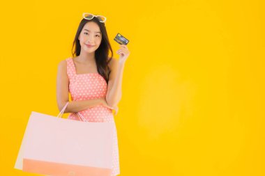 Renkli alışveriş çantalı güzel Asyalı kadın akıllı cep telefonu ve sarı izole edilmiş arka planda kredi kartı.