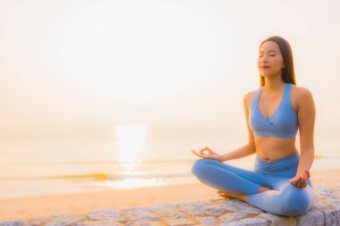 Genç Asyalı kadının portresi sağlık için gün doğumunda deniz kıyısı okyanusunda meditasyon yapıyor.