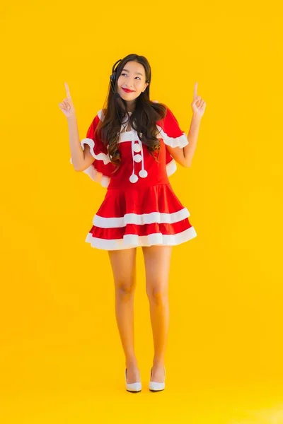 Portrait beautiful young asian woman wear christmas clothes and hat with headphone or headset for call center on yellow isolated background