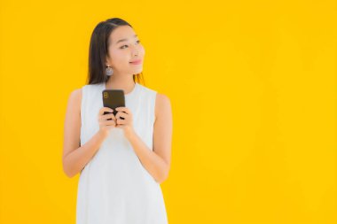Sarı izole edilmiş arka planda akıllı cep telefonlu güzel Asyalı kadın portresi