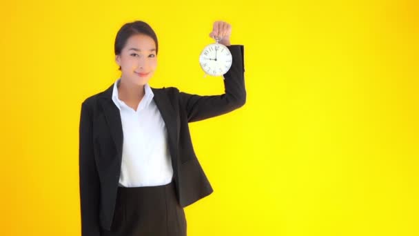 黄色の背景に目覚まし時計を持つ美しい若いアジアの実業家の映像 — ストック動画