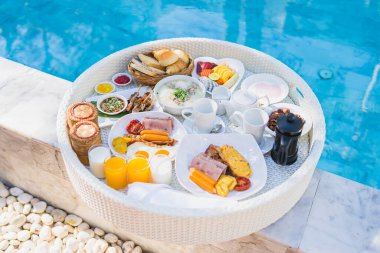 Kızarmış yumurta omletli, jambonlu, meyveli, sütlü kahveli ve yüzme havuzlu bir tepside yüzen kahvaltı.