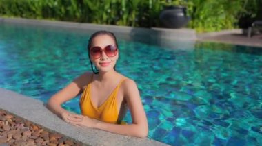 Güzel Asyalı bir kadının, tatil için otel tatil beldesinde yüzme havuzunda dinlendiği görüntüler.