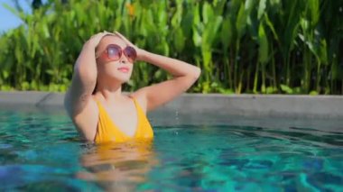 Güzel Asyalı bir kadının, tatil için otel tatil beldesinde yüzme havuzunda dinlendiği görüntüler.