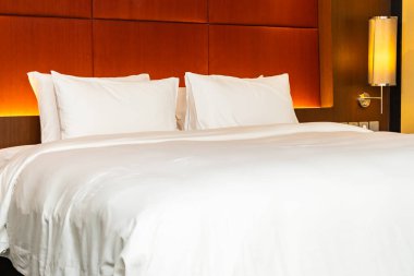 Beyaz yastık ve battaniye yatak odasının içinde lamba süslemesi olan yatakta.