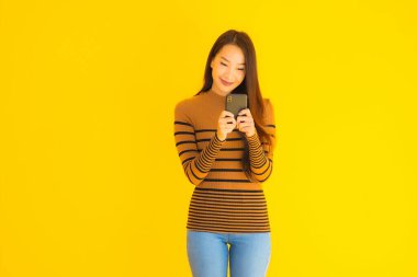 Güzel genç Asyalı kadın, sarı izole edilmiş arka planda birçok eylem içeren akıllı cep telefonu ya da cep telefonu kullanır.