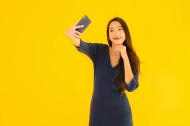 Akıllı cep telefonlu güzel Asyalı kadın portresi ya da sarı izole edilmiş arka planda cep telefonu.