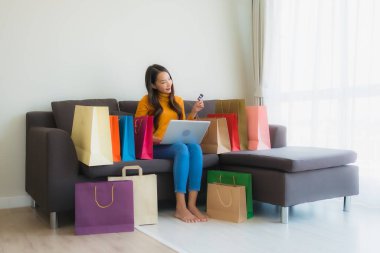 Genç Asyalı kadının oturma odasında online alışveriş yapmak için akıllı cep telefonu ve kredi kartı olan dizüstü bilgisayarı kullandığı portre.