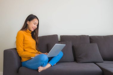 Genç Asyalı bir kadının oturma odasında çalışmak için dizüstü bilgisayar defteri kullanmasının portresi.